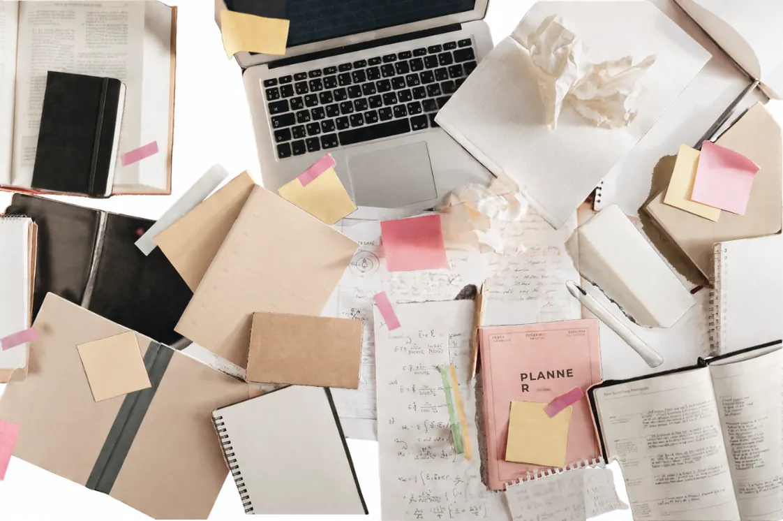 Een bureau vol notitieboeken, briefjes en een laptop.