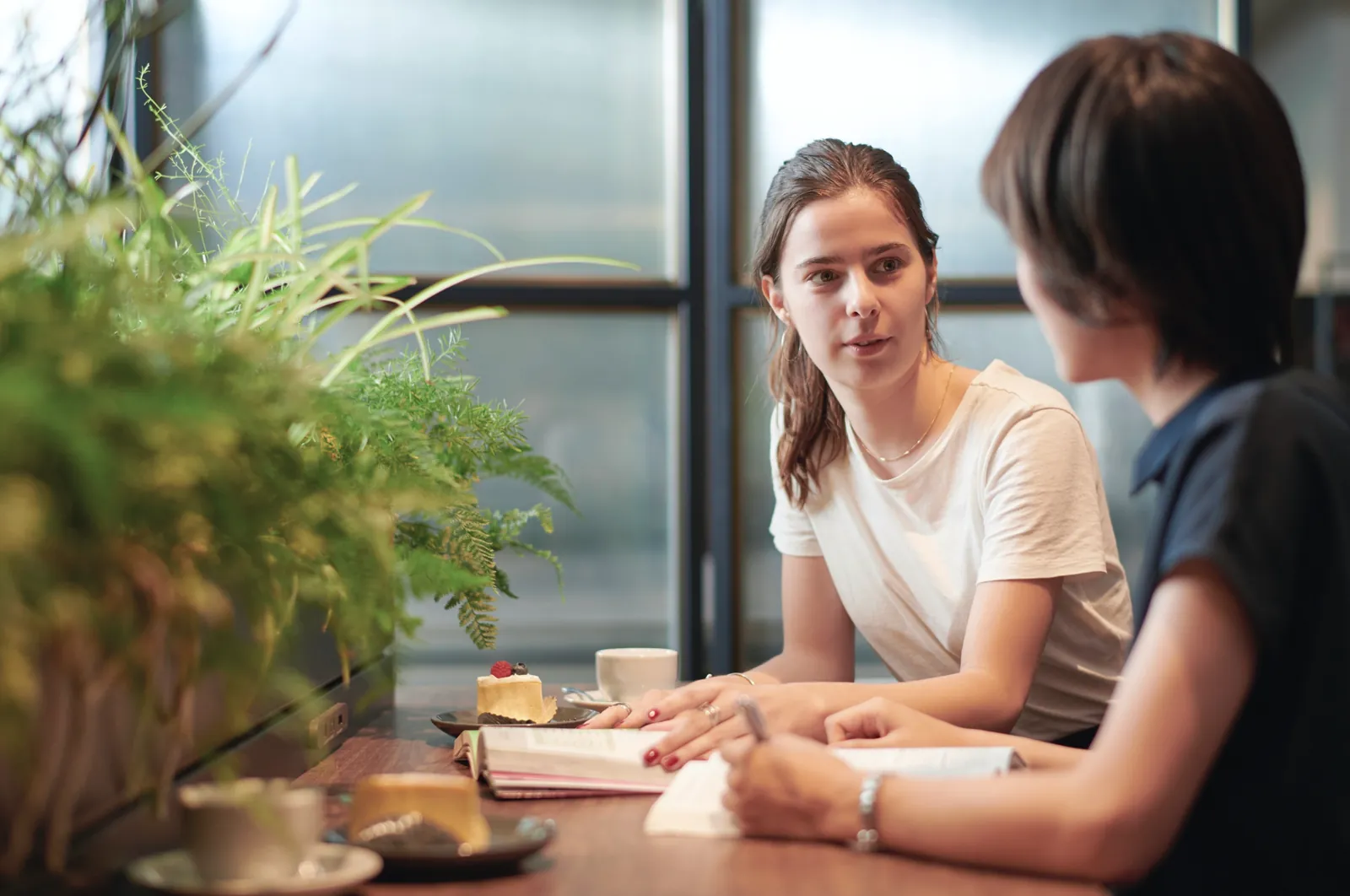 Twee collega's in gesprek aan een tafel bij het raam.