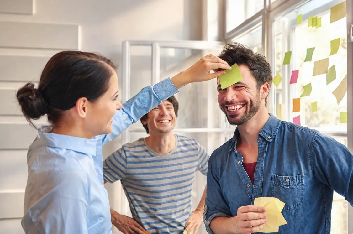 Collega's lachen samen bij een raam vol plaknotities.